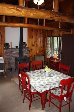 Living/dining area with log beams, woodstove, seating, access to the front porch