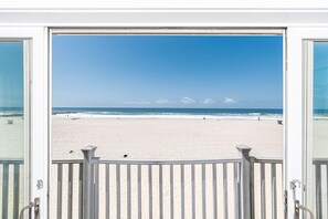 Sliding doors open to the front balcony with panoramic views of the pedestrian boardwalk, beach, and ocean beyond.
                