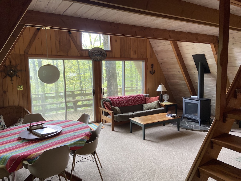 Interior of cabin with living area, dining table, wood stove, and deck. 