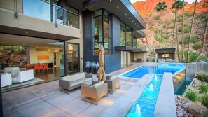 Modern villa with balcony, pool, hot tub, and mountain views at twilight.