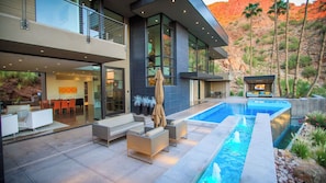 Modern villa with balcony, pool, hot tub, and mountain views at twilight.