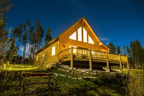 Bear Crossing Cabin lit up at night with custom cedar bench and large deck