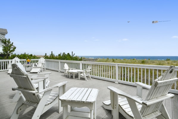 Large oceanfront deck with Adirondack chairs overlooks a beautiful dune  & beach