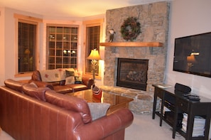 Great room with flatscreen TV and gas log fireplace overlooking deck and slopes.