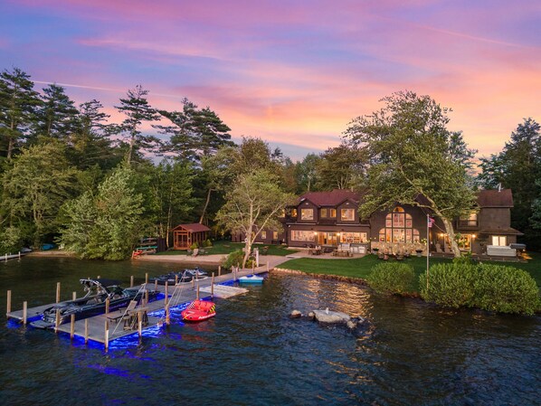 Drone view of lakeside of property including beach, dock and landscaping.