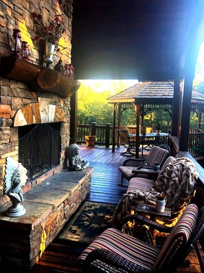 Covered top balcony with seating area around wood burning fireplace & gas grill