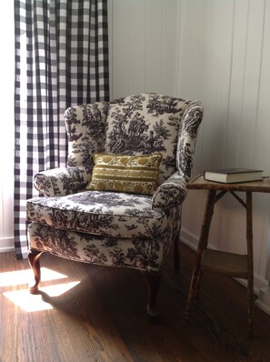 Toile covered wingback chair and an antique bamboo table on wide plank floors.