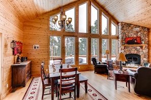 The beautiful great room has high vaulted ceilings and two-story windows. There is a large stone wood-burning fireplace.