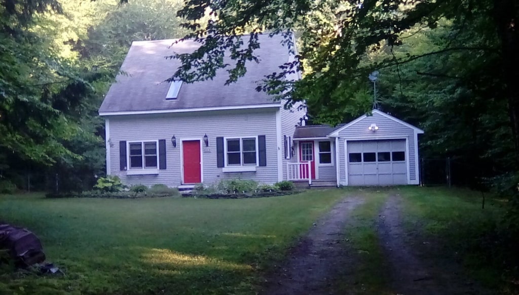 A vacation home in Stowe, Vermont sits at the end of a driveway with a lush green lawn in front and dense greenery surrounding it on a sunny summer day.