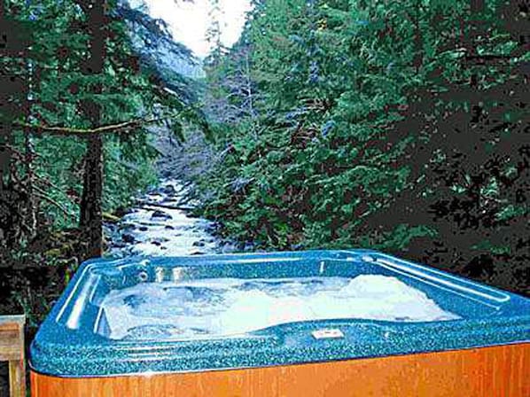 Large hot tub at edge of view deck overlooking river and forested mountains