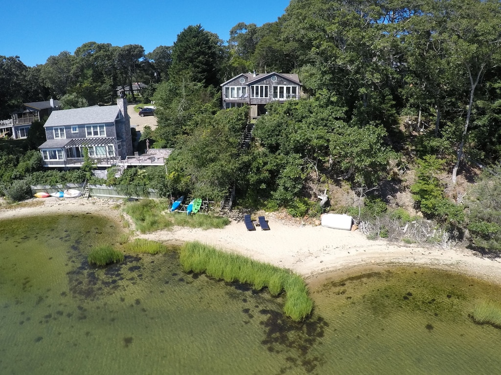 Vacation rentals in Martha's Vineyard are seen from an aerial view with a private beach and dense greenery surrounding them under a blue sky.
