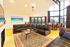 The open-plan living space features soaring cathedral ceilings, a cosy log fire, and large picture windows that frame the scenic views, creating a warm and inviting atmosphere.