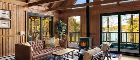 Lovely great room affords beautiful views of the lake, opens on to the screened porch (left) and the hot  tub (center), has a wood burning stove and a 50" Amazon Fire TV