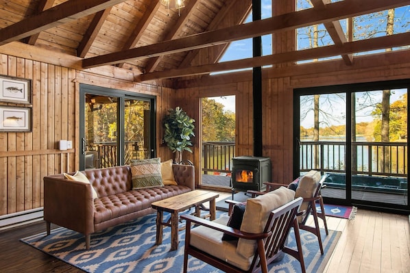 Lovely great room affords beautiful views of the lake, opens on to the screened porch (left) and the hot  tub (center), has a wood burning stove and a 50" Amazon Fire TV