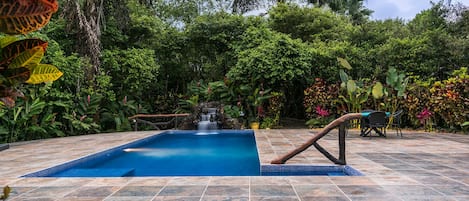 Swimming pool with waterfall and wood-designed railing.