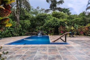 Swimming pool with waterfall and wood-designed railing.