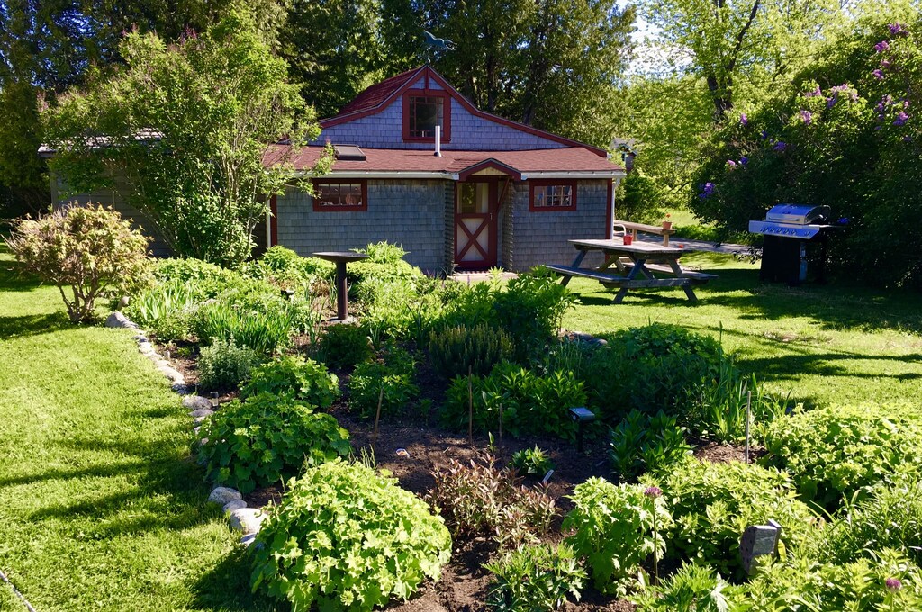 A popular Acadia vacation rental is seen with a gorgeously landscaped garden in front with a picnic table and lush greenery all around