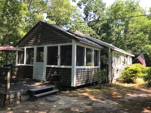 Side of cottage, deck with table, chairs, umbrella.