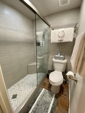 Newly renovated walk-in tiled shower with glass doors, bench & private toilet