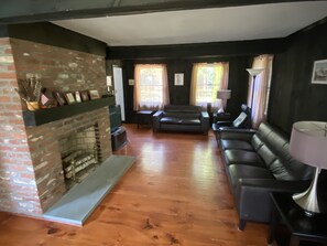 Living room has leather couch, loveseat, chair, flat screen TV, and fireplace.
