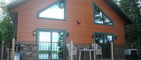 Cabin facing lake, deck with table, chairs, and grill.