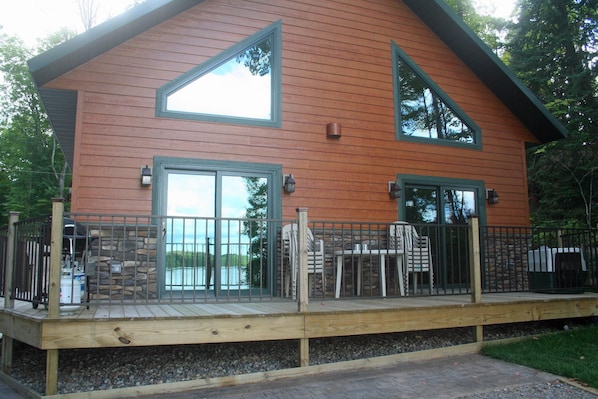 Cabin facing lake, deck with table, chairs, and grill.