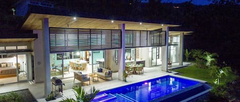 Evening Illumination Shows Large Pool and Integrated Deck, Lounge, Kitchen.