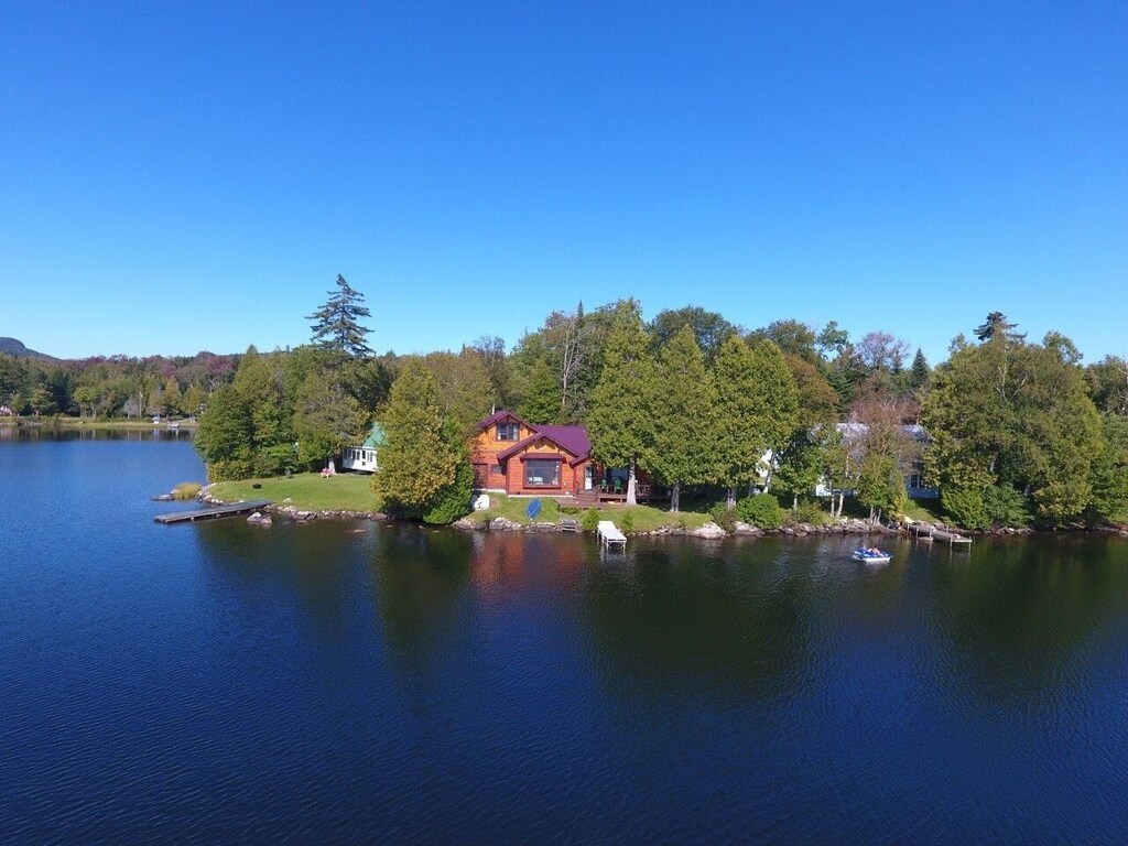 Aerial view of a waterfront Vermont cabin with deep blue water in front and forests behind