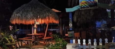TIki Hut from sidewalk at night with big shell front yard and massive Palm trees