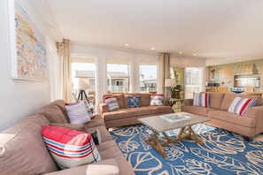 The bright and cheery living area includes sofa/loveseat set, side seating, cable TV, and sliding glass door that opens to spacious ocean view deck