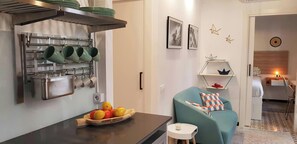 This open-plan living area features a stylish, teal sofa with geometric patterned cushions. The adjacent bedroom is visible through an open doorway, with a simple yet elegant wooden headboard and bedside lamp. This apartment is designed for those who valu