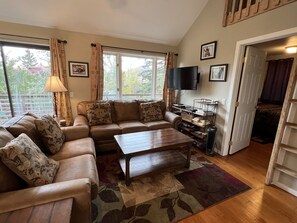 Living room with vaulted ceiling and open floor plan, HD TV, door to deck.