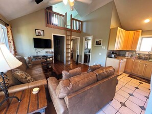 Living room with vaulted ceiling and open floor plan, HD TV, door to deck.
