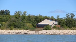 Cottage is steps away from the water with grass and sandy area for sitting.