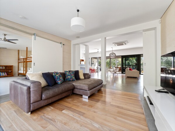 The second living area offers a leather sofa, a large screen, and a leafy outlook, perfect for films or quiet time.