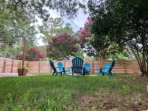 Spacious, shady backyard with fire pit and high fence for privacy.