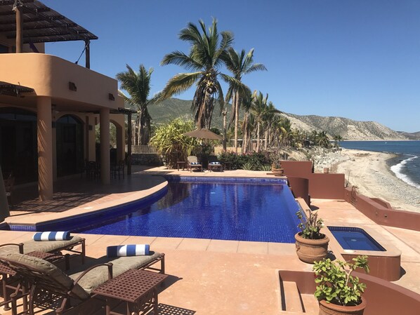 View of backyard patio w/ sunning chairs, infinity edge pool & large Jacuzzi.