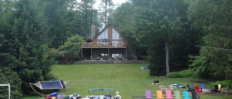 View from the lake of house, chairs, fire pit and lake toys