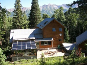 Backside of the home surrounded by trees and a view of the mountains.
