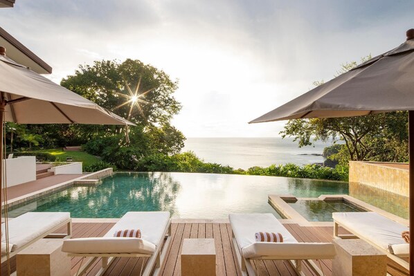 Oceanfront pool with comfortable lounge chairs and shaded umbrellas