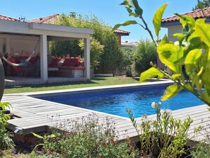 La piscine en premier plan puis le pool house en fond avec ses banquettes
