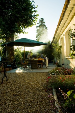 Terrasse avec tables en béton, et barbecue sous  les platanes