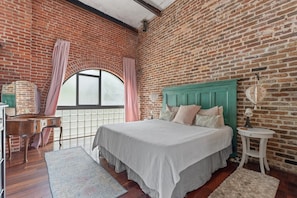 Master Bedroom with 15' ceiling heights, brick walls and arched window.