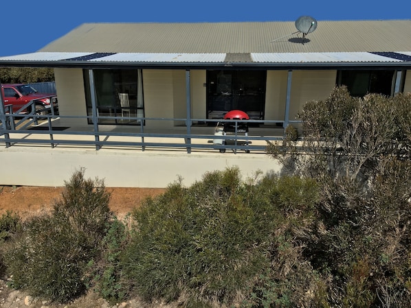 Front of house and covered deck set amongst lush coastal vegetation