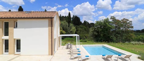 Esterno della casa. La tettoia e un ombrellone creano ombra nella terrazza