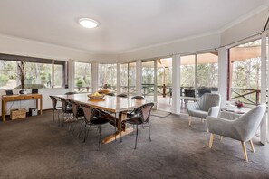 The dining area is surrounded by floor-to-ceiling windows, allowing natural light to pour in and providing direct access to the outdoor deck.