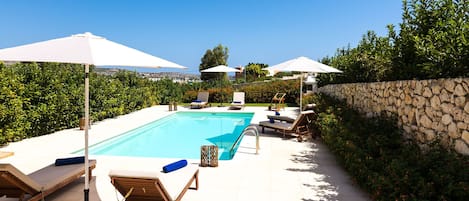 35 sqm Swimming pool with sun beds & umbrellas surrounded by trees & flowers
