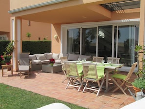 Terras aan tuinkant met lounge in twicker, deckchair, tafel en stoelen in teak