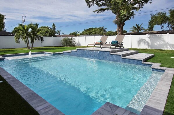 Sparkling pool surrounded by artificial turf in wide-open back yard