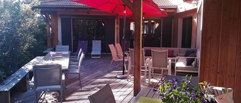 Terrasse avec coin repas et espace farniente au salon d'été sous les parasols. 